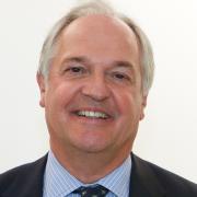 Photo of a white man in a blue shirt and tie smiling.